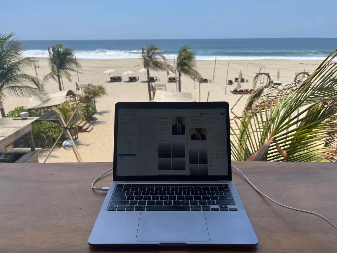 Patrick's laptop on a wooden desk overlooking a beach lined with palm trees.